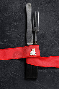 情人节桌布置用刀叉红丝带黑色背景顶端视图片