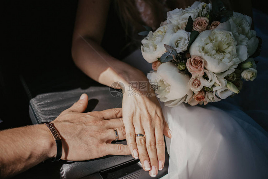 新婚夫妇的手互相接触手与结婚戒指的新婚夫妇关闭汽车座椅上的黑色皮革扶手上有戒指的新娘手因图片