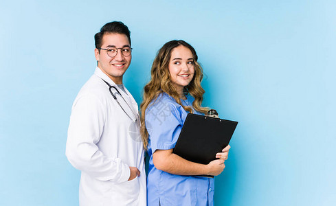 穿着蓝色背景的年轻医生夫妇被孤立地抛在一边微笑图片