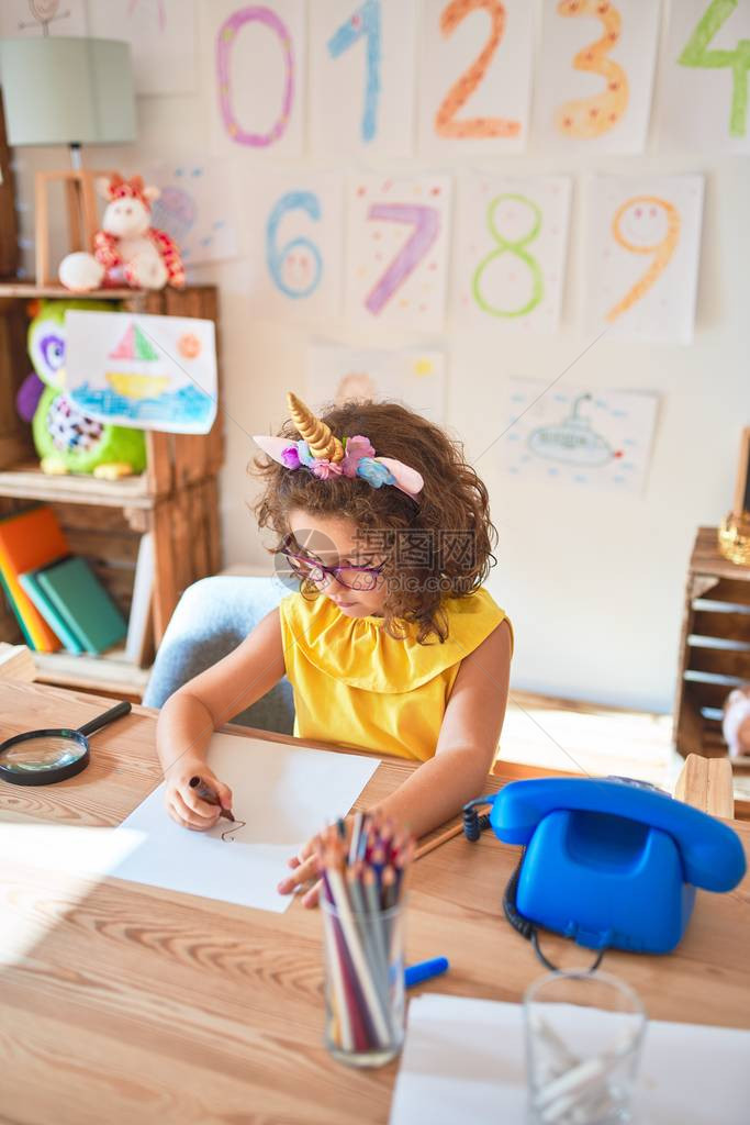 在幼儿园用纸笔和标志笔坐在桌边绘画时图片