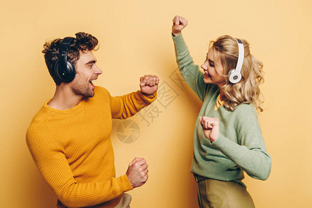 在黄色背景下用无线耳机听音乐时跳舞的快乐男人图片