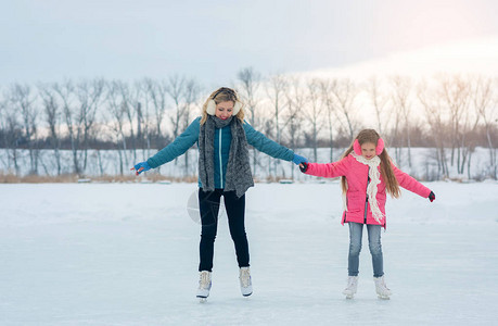 微笑的年轻母亲和她可爱的女儿一起用手滑冰家庭滑冰和训练在冬日在冰区的白色溜冰鞋周末在寒冷天气背景图片