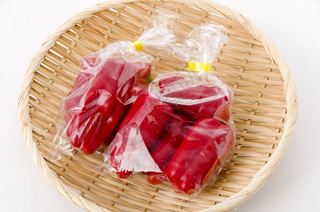 白色背景竹滤器上塑料袋中的红甜椒图片