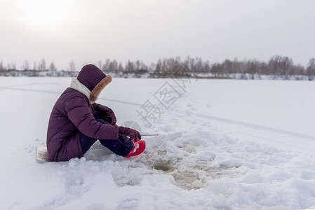 一个孤独的钓鱼女孩正专注于用一根冬季钓鱼竿钓鱼图片