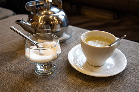 泡茶用的金属茶壶白陶瓷杯咖啡馆桌上的图片