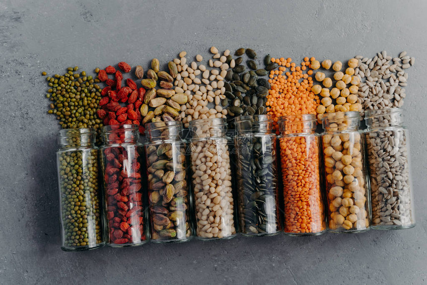 透明玻璃罐中的有机谷物坚果种子的室内镜头洒在灰色的表面上食品包装储存素食者的健康图片