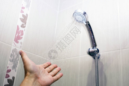 男和淋浴头的水流下检查水温选择焦点图片
