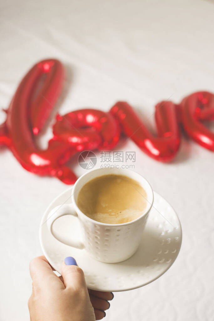 一杯女手的咖啡在红宝石气球的背景上以爱这个词的形状情人节的概图片