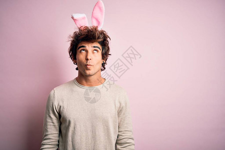 长着复活节兔子耳朵的英俊男青年站在孤立的粉红色背景上图片