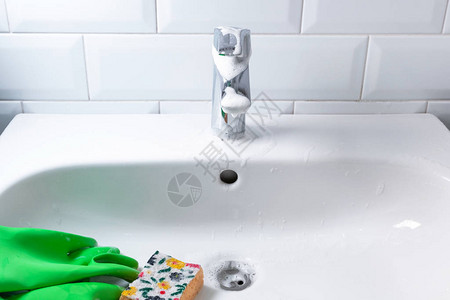 带绿色橡胶手套和黄色海绵的陶瓷浴盆图片