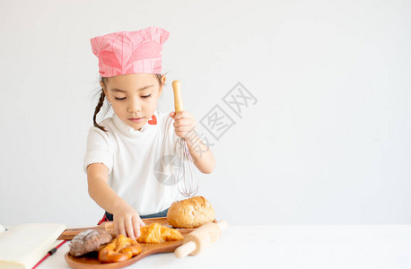 亚洲小厨师女孩展示了快乐和趣的动作与面包和蛋糕烹饪背景图片