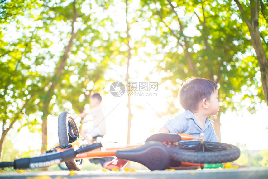 亚洲男孩在公园树林露户活动的公路上因自行车事故而摔落平图片