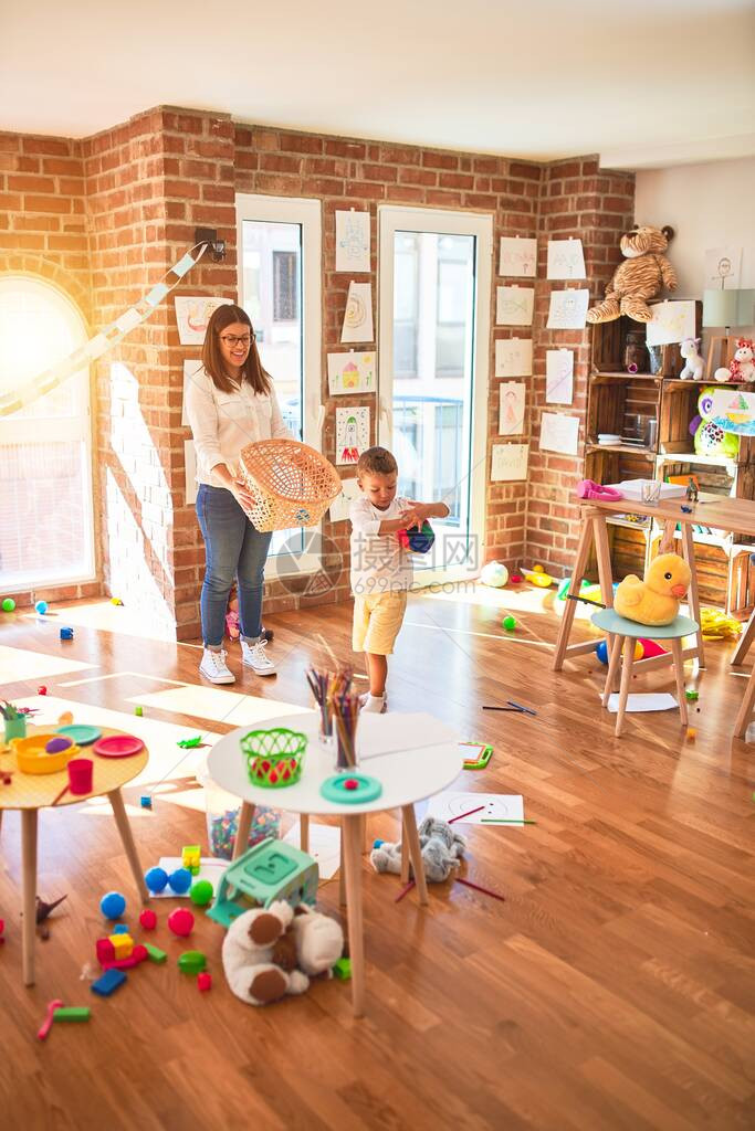 漂亮的老师和幼儿在幼儿园的许多玩具周围用球和图片