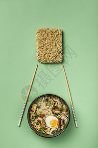 有蘑菇鸡蛋豆腐奶酪筷子和原料的面条碗绿色背景图片