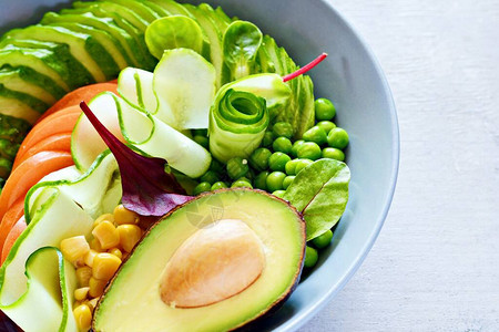 新鲜蔬菜黄瓜番茄玉米青豆鳄梨蓝底的碗里生菜健康饮食概念图片