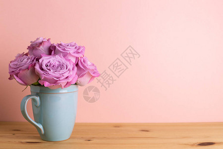 粉红色背景的木制桌边陶瓷杯中的紫玫瑰花朵图片