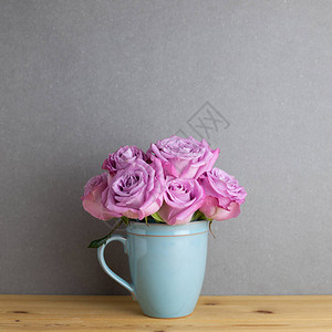灰色背景的木制桌椅上陶瓷杯中的紫玫瑰花朵图片