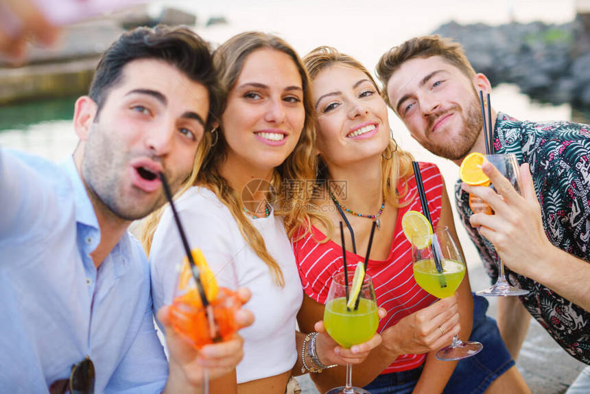 一群在海边玩乐用智能手机拍自喝彩色鸡尾酒的好朋友团体图片