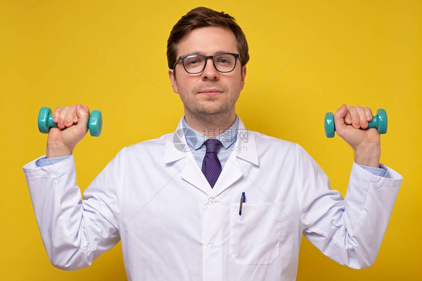 持有哑铃就健康生活方式提供咨询的成熟的caucasian男医生黄墙上的体图片