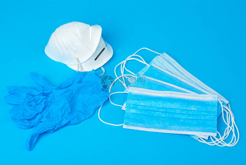 蓝色背景上带有白色橡皮筋的无纺布材料制成的一次手套和一叠医用口罩图片