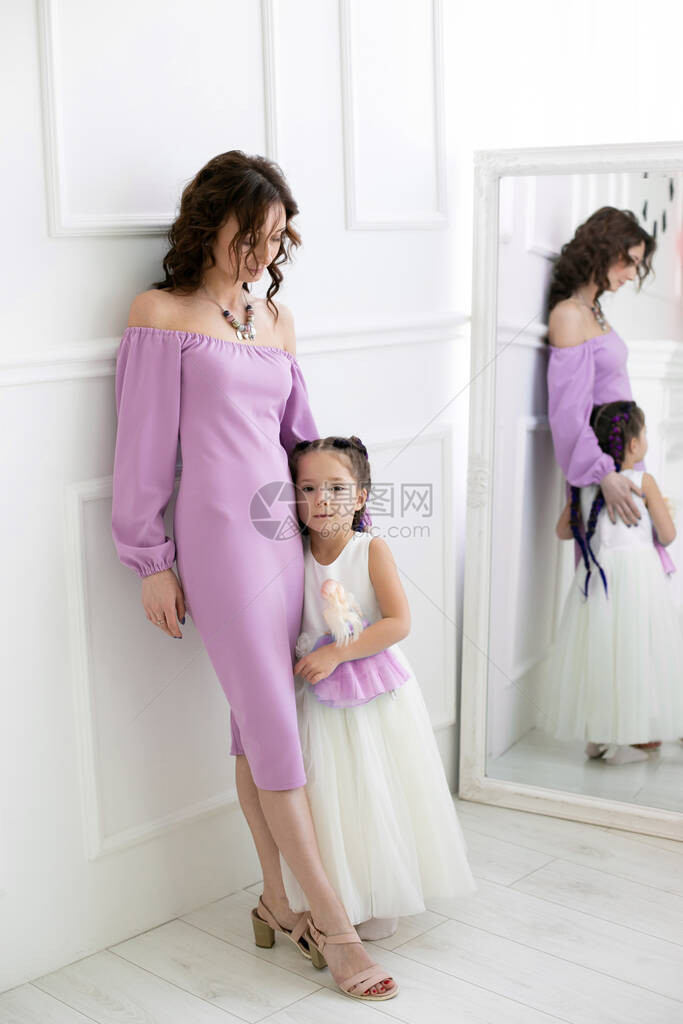 身着紫色裙子的年轻苗头女子和5岁女儿站在镜子附近的一个图片