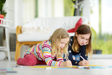 两个年轻的姐妹在家里用彩色铅笔画有创意的孩子一起做手工艺品孩子们的教育和远程学习隔离期间在家上学背景图片