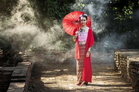 在烟雾中穿着带雨伞的泰式传统服装的美丽的泰国妇女图片