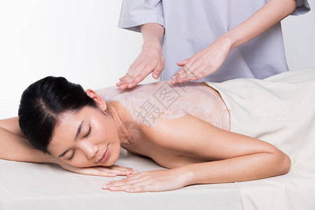 在健康水疗中心对亚洲女皮肤进行轻柔的红拍草本美容护理背景图片
