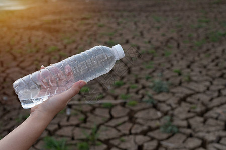 近身女手握着裂土背景的透明塑料瓶图片