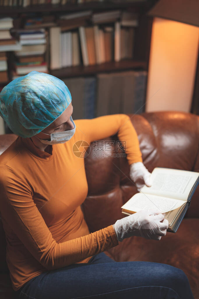 带着保护抗面具的妇女单独坐在家中隔离和阅读书图片
