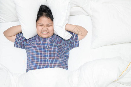肥胖的男孩躺在床上用枕头捂住头图片