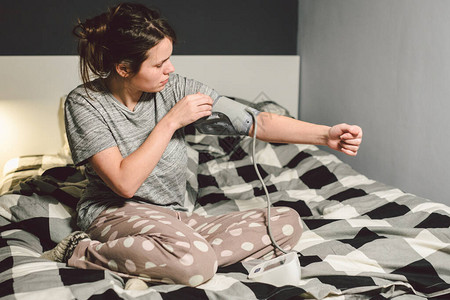 题目高血压高血压病22岁的年轻白种人妇女使用自动眼压计她把袖口放在胳膊上检查压力回家在卧室的床背景