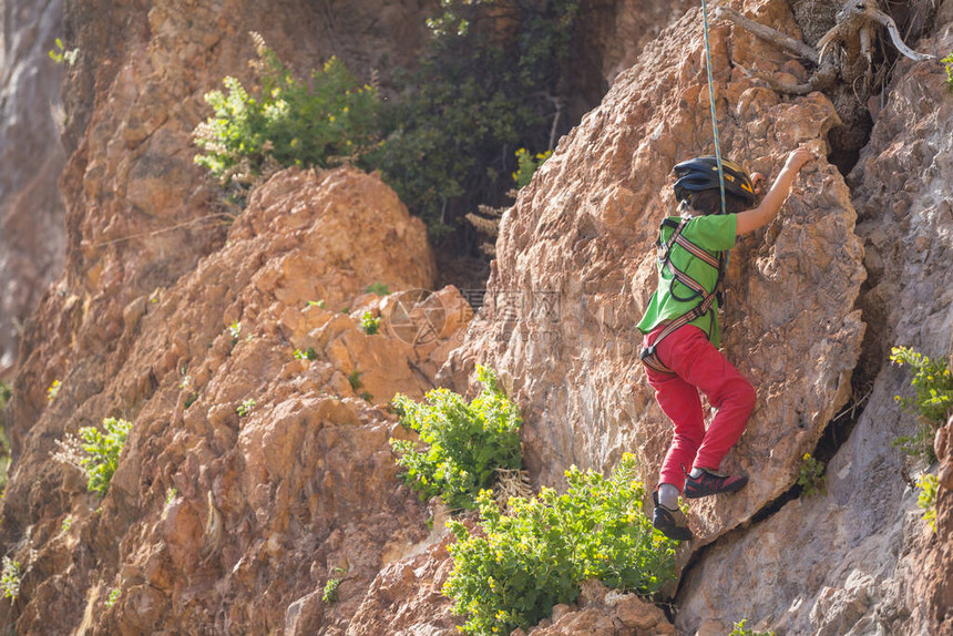 一个戴头盔的男孩在山上攀岩极度爱好运动健壮的孩子要坚强起来岩石爬的也非常高啊图片
