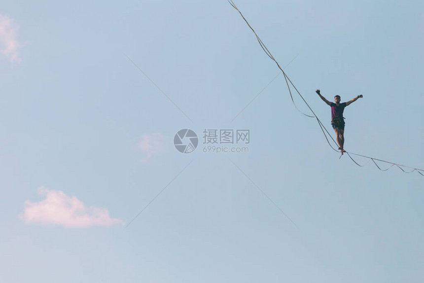 以蓝天为背景的Highliner做出了动作一个人正沿着一条拉长的吊索行走能走钢丝人在深渊中保持平衡向前迈出了图片