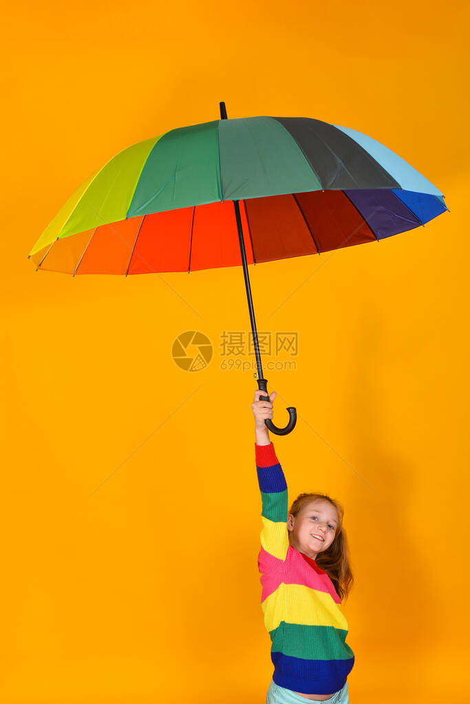 身穿彩色毛衣的女孩手上握着多色雨伞在黄色背景一个孩子和图片