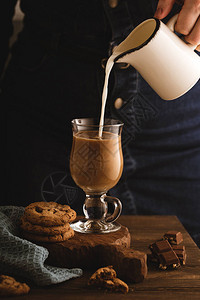 女人把牛奶倒进玻璃杯里加咖啡茶歇组合与一杯咖啡饼干和巧克力色调的照图片