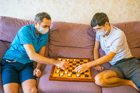 戴着防护面具的爸和十几岁的儿子玩跳棋图片