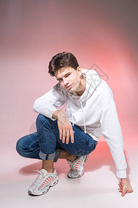 时尚英俊的年轻欧洲男模特身着白色运动衫蓝色牛仔裤和白色运动鞋图片