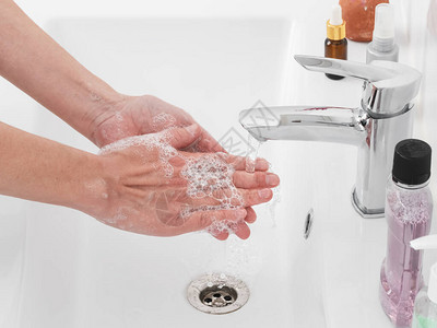 女人在浴室的水龙头下用肥皂洗手图片