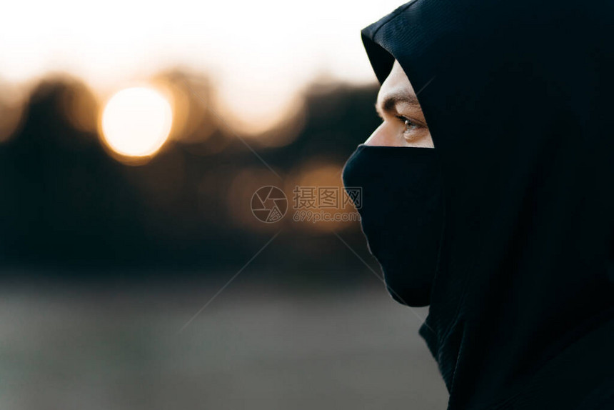 戴着黑色医用流感口罩和运动黑色连帽衫的年轻悲伤男子的脸型图片