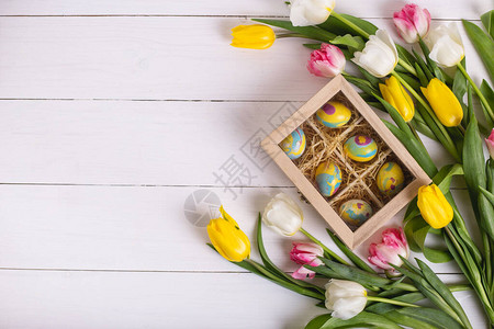 白色木制桌和郁金香的长木盒子中的稻草床上彩色东方鸡蛋的最顶端视图图片