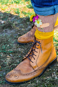 男人穿着黄色鞋子的双腿站在绿色的草地上黄色和粉红色的春天花朵用背景图片