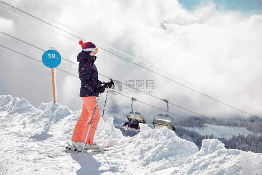 站在滑雪斜坡山丘和背景椅子上的年轻女子滑雪运动员图片