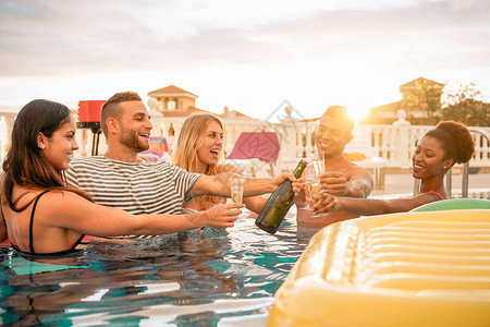 快乐的朋友在泳池派对上举杯庆祝年轻人在日落时在豪华热带度假村喝起泡酒玩得开心暑假和期青年背景图片