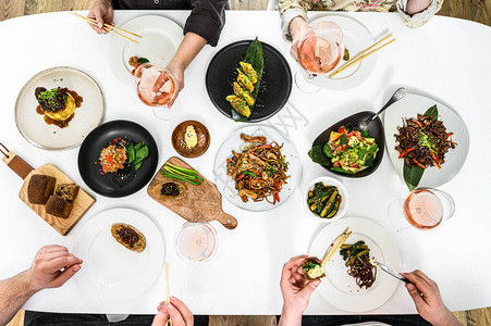 家人朋友聚餐吃烤鸭饺子春卷炒面沙拉蔬菜喝酒的人手庆祝晚宴白色图片