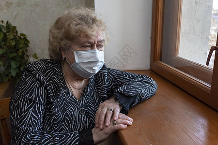 一名戴保护面罩的老年妇女坐在家中图片