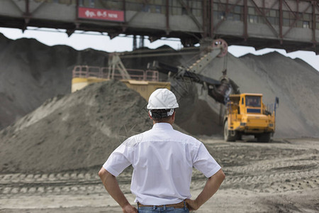 身穿白衬衫和头盔的采矿工程师在采矿设备和挖掘机中监督花岗岩加图片