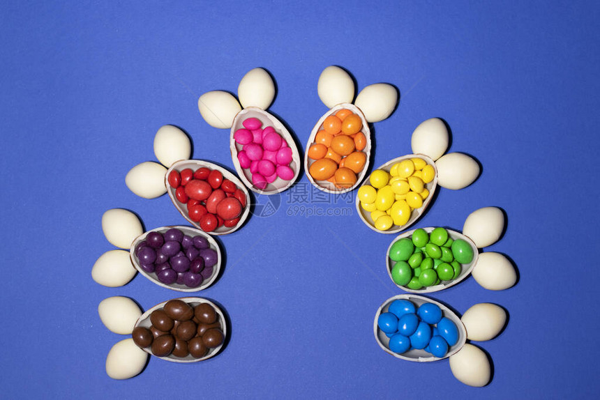由巧克力蛋和彩色果冻制成的兔子在蓝色背景上形成一个半圆形每只兔子都对应一种颜色的果冻照片由平躺拍摄图片
