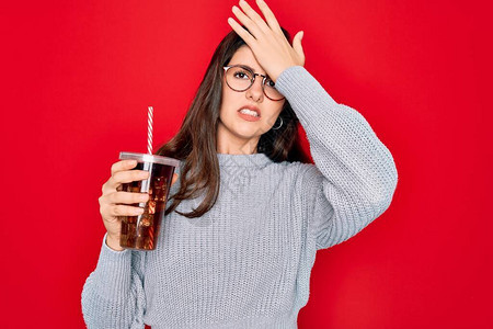 身戴眼镜的年轻美女在红色背景下喝着甜饮料苏打水图片