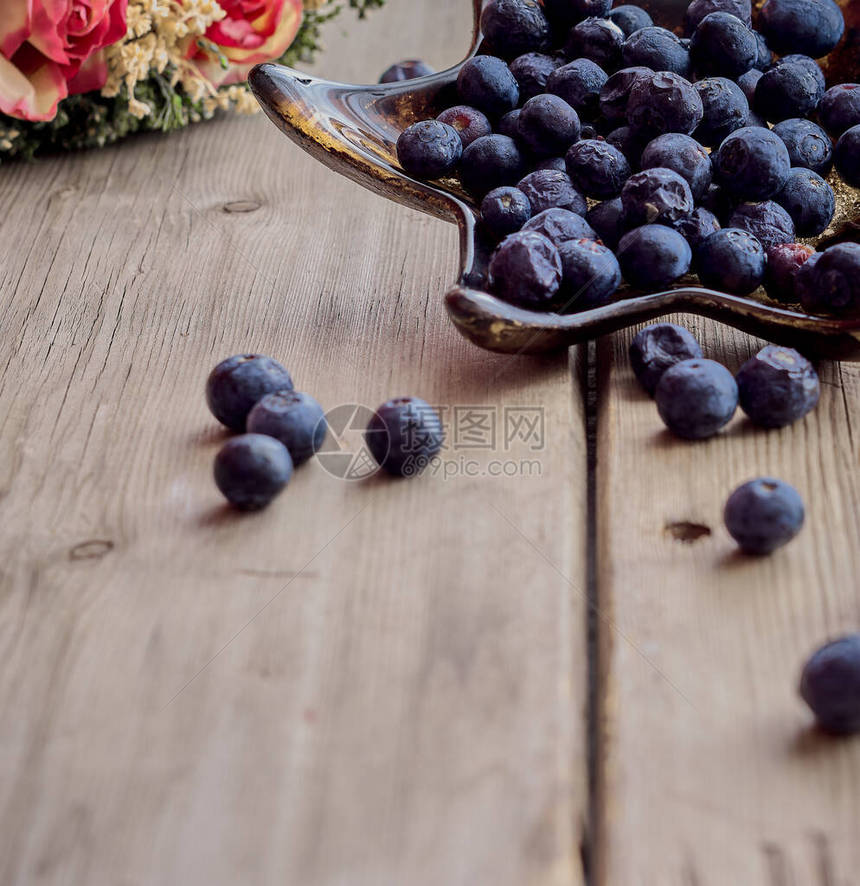 木板上的盘子上的一堆蓝莓和几朵花图片